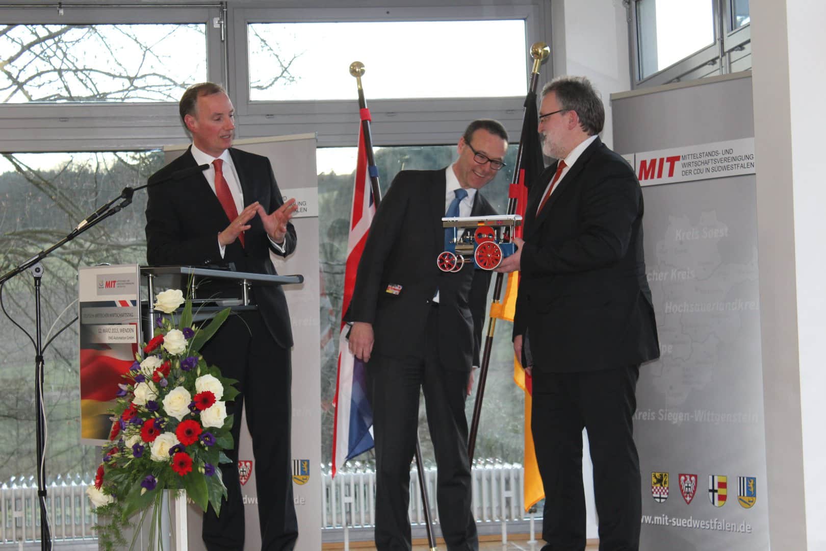 Foto: Dr. Matthias Heider (links) und MIT-Kreisvorsitzender Markus Scherer (rechts) übergaben dem britischen Botschafter als Andenken eine Dampfmaschine "Made in Südwestfalen". Foto: Sven Oliver Rüsche (sor)