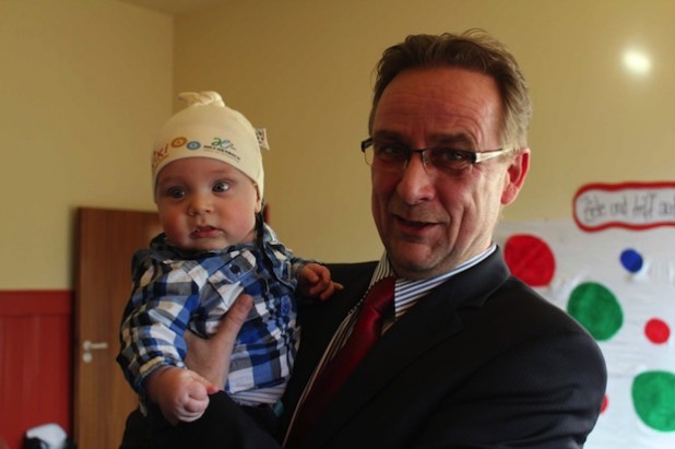 Die Wiki-Mütze ist modisch attraktiv, wie der sieben Monate junge Sanel Catic auf dem Arm des Bürgermeisters beweist (Foto: Stadt Hilchenbach).
