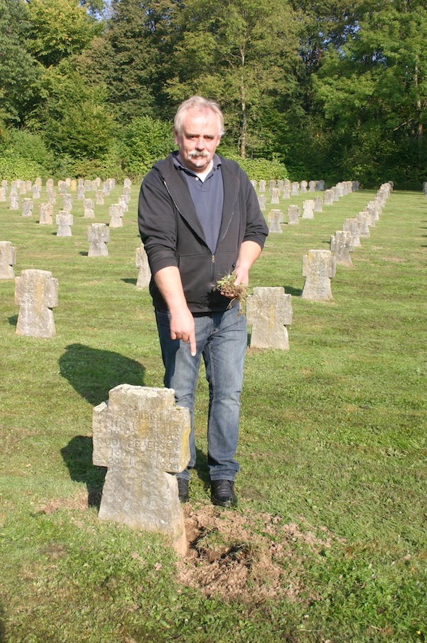 Friedhofsverwalter Reinhard Paul zeigt auf einen Grabstein, der von freilaufenden Hunden auf dem Ehrenfriedhof teilweise ausgebuddelt wurde (Foto: Stadt Meschede).