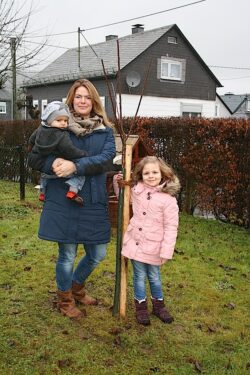 Frisch gepflanzt! Das Süßkirschenbäumchen für den kleinen Felix wird nun in Altenseelbach Wurzeln schlagen. Das freut auch Verena und Stella Meyer (Foto: Gemeinde Neunkirchen).