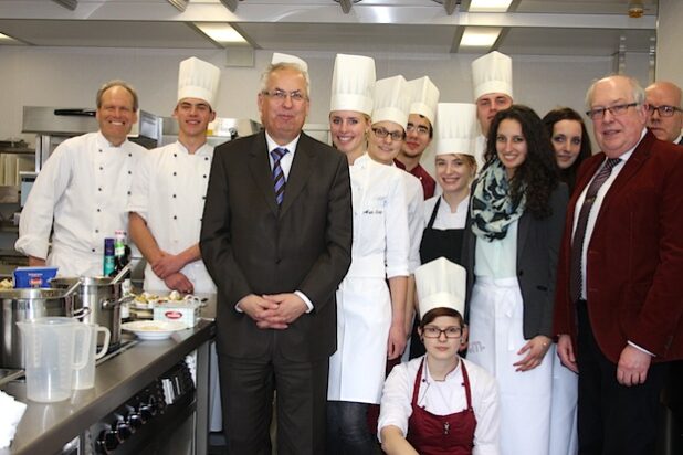 Landrat Dr. Karl Schneider (M.) und Schulleiter Jürgen Kriegel (vorne, r.) nahmen, eingerahmt von den Auszubildenden, einen Blick in die neue Lehrküche am Berufskolleg Meschede (Foto: Pressestelle Hochsauerlandkreis).