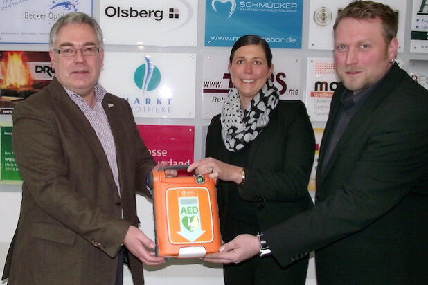 „Defi“ für die Konzerthalle Olsberg: Cathrin Kreutzmann von der Sparkasse Hochsauerland und Tobias Klauke vom Förderverein der Schützenbruderschaft St. Michael Olsberg überreichten das Gerät jetzt an Bürgermeister Wolfgang Fischer (Foto: Stadt Olsberg).