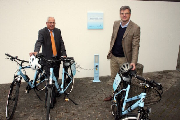 Landrat Dr. Karl Schneider (l.) und Frank Eikel, Leiter Hauptregion Südwestfalen/Sieg der RWE, nahmen die neue E-Bike-Ladestation am nördlichen Eingang des Henneparks in unmittelbarer Nachbarschaft zum Kreishaus Meschede in Betrieb. Gleichzeitig erhielt der Hochsauerlandkreis drei E-Bikes, die künftig für Dienstfahrten bei kurzen Strecken genutzt werden können (Foto: Pressestelle HSK).