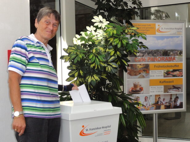 Ingrid Hetzler hat als eine der ersten Patientinnen die Befragung dankbar angenommen und den Umschlag in die Einwurfbox eingeworfen (Foto: St. Franziskus-Hospital gGmbH).