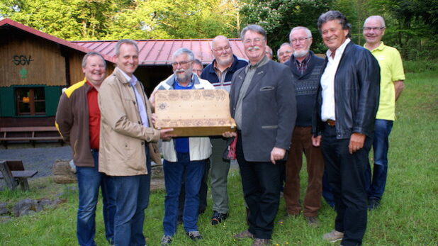 Übergabe des SGV-Schnadeholzes von Klaus Meier (MGV, rechts) an Andreas Düllberg (SV 09, links) auf dem Außengelände der SGV-Hütte "Hermann Balkenohl" im Hellefelder Bachtal. Hinter dem Schnadeholz Gerd Riedel (SGV). Dritter von rechts: Heiko Balkenohl - Foto: Klaus Peters.