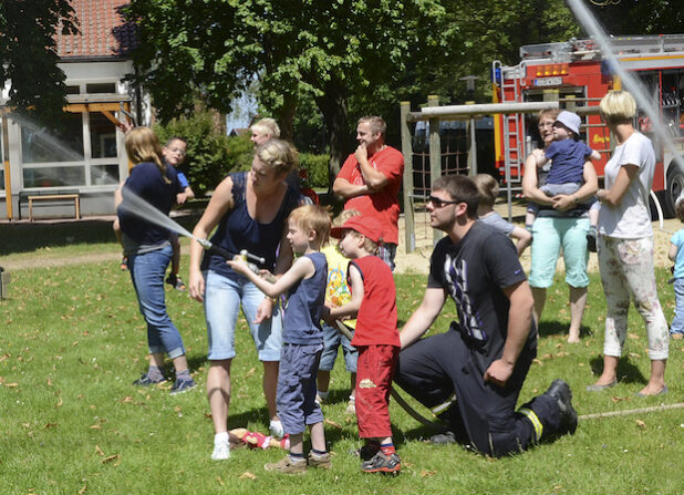 Begeistert löschen die Zwergenlandkinder unter Anleitung von Micha Kleinschmidt und Martin Aßhauer mit dem Feuerwehrstrahlrohr einen fiktiven Brand (Foto: Thomas Weinstock/Kreis Soest).