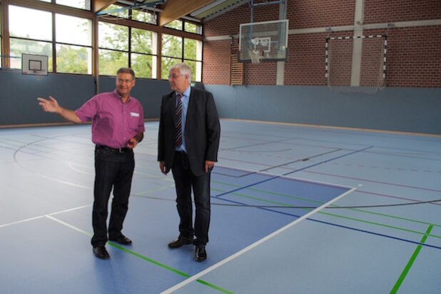 Dipl.-Ing. Peter Temmhoff (li.) stellt Bürgermeister Uli Hess den neuen Sportboden der Turnhalle am Rautenschemm vor. Bildnachweis: Stadt Meschede