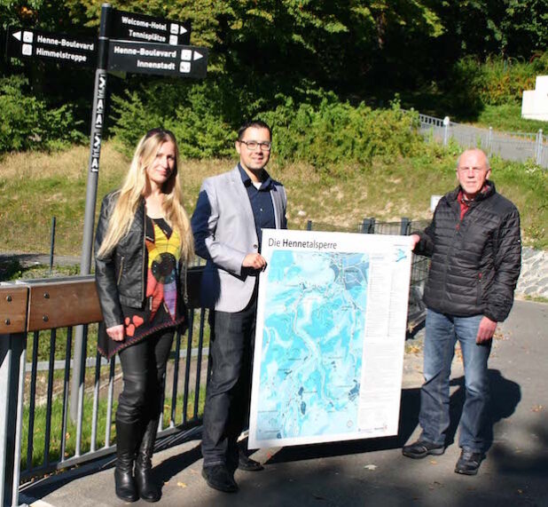 Hilke Brake und Stephan Rach vom Fachbereich Planung und Bauordnung sowie Christof Sommer vom Ruhrverband mit einem der neuen Hinweisschilder, die rund um den Hennesee aufgestellt werden (Foto: Stadt Meschede).